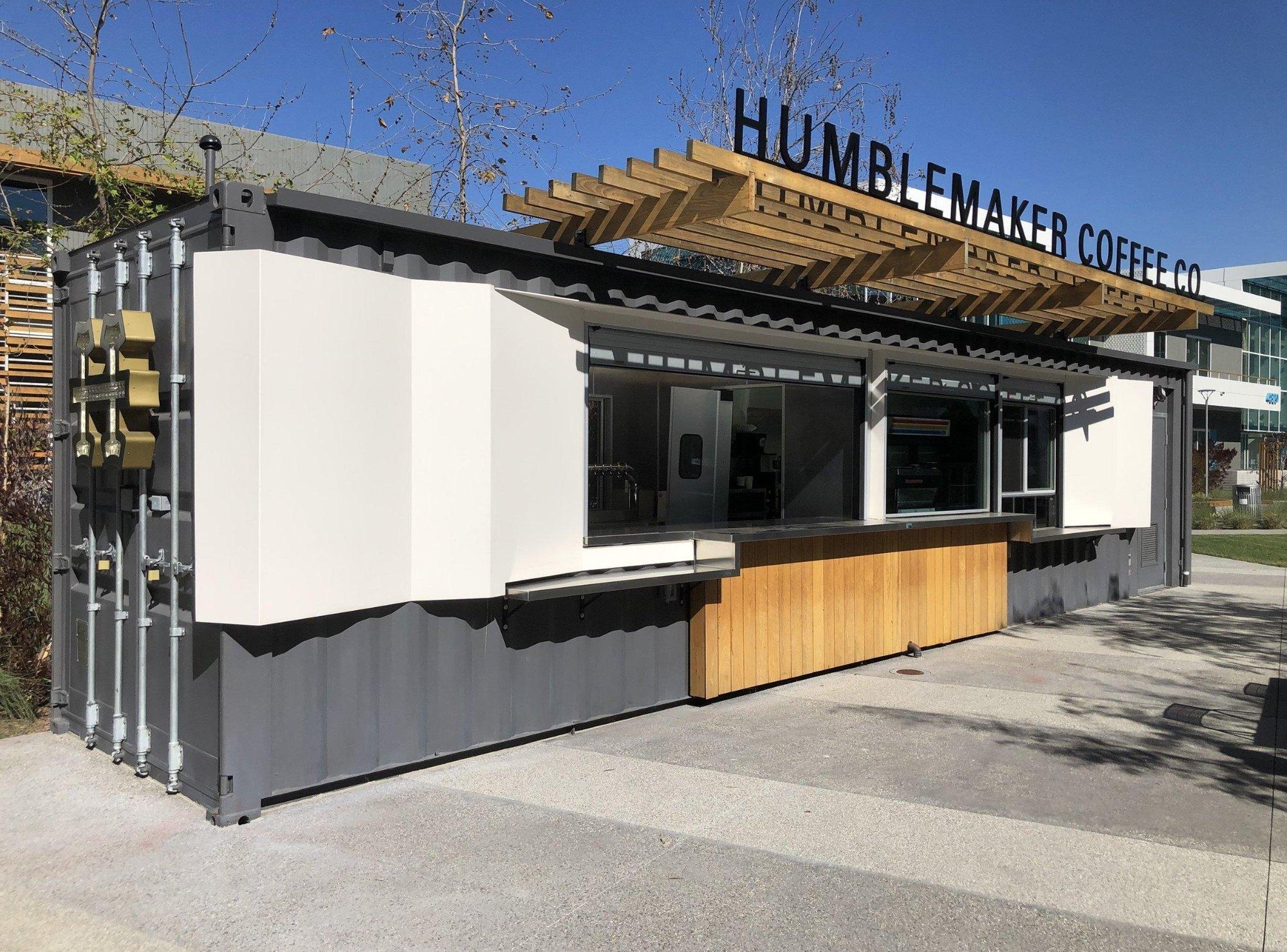 Gray container coffee kiosk with a white fold-out window shroud and wood slat canopy